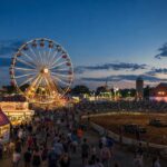 DC Spot editorial illustration of a summer county fair midway with a Ferris wheel and demolition derby arena