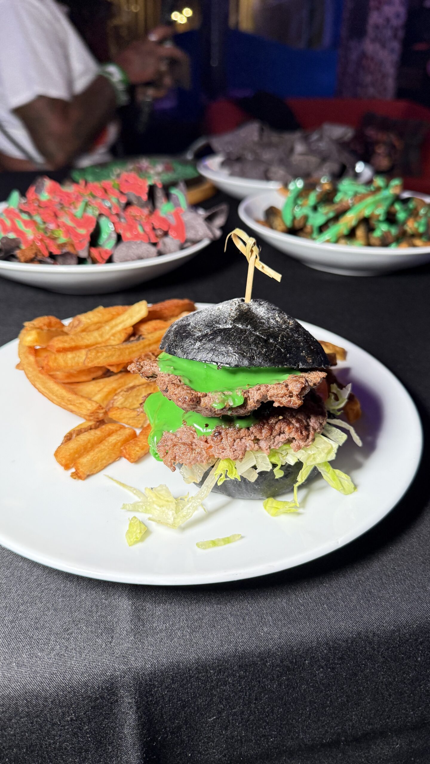 Black-bun burger with green sauce and fries from the 2025 Frankenstein cocktail lab menu at Puttery