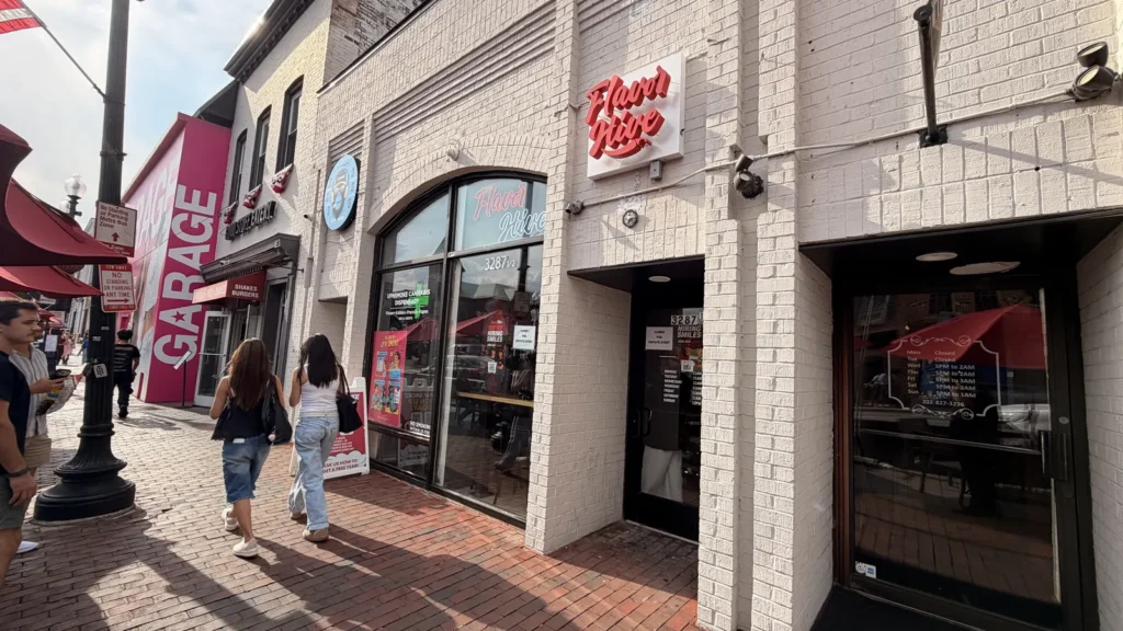 Flavor Hive’s red neon sign above its white brick storefront on M Street in Georgetown, with shoppers walking the brick sidewalk