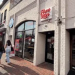 Flavor Hive’s red neon sign above its white brick storefront on M Street in Georgetown, with shoppers walking the brick sidewalk