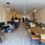 Guests ordering inside Habibi House Cafe in Falls Church, with arched alcoves, rattan pendant lights, green banquettes and long communal tables