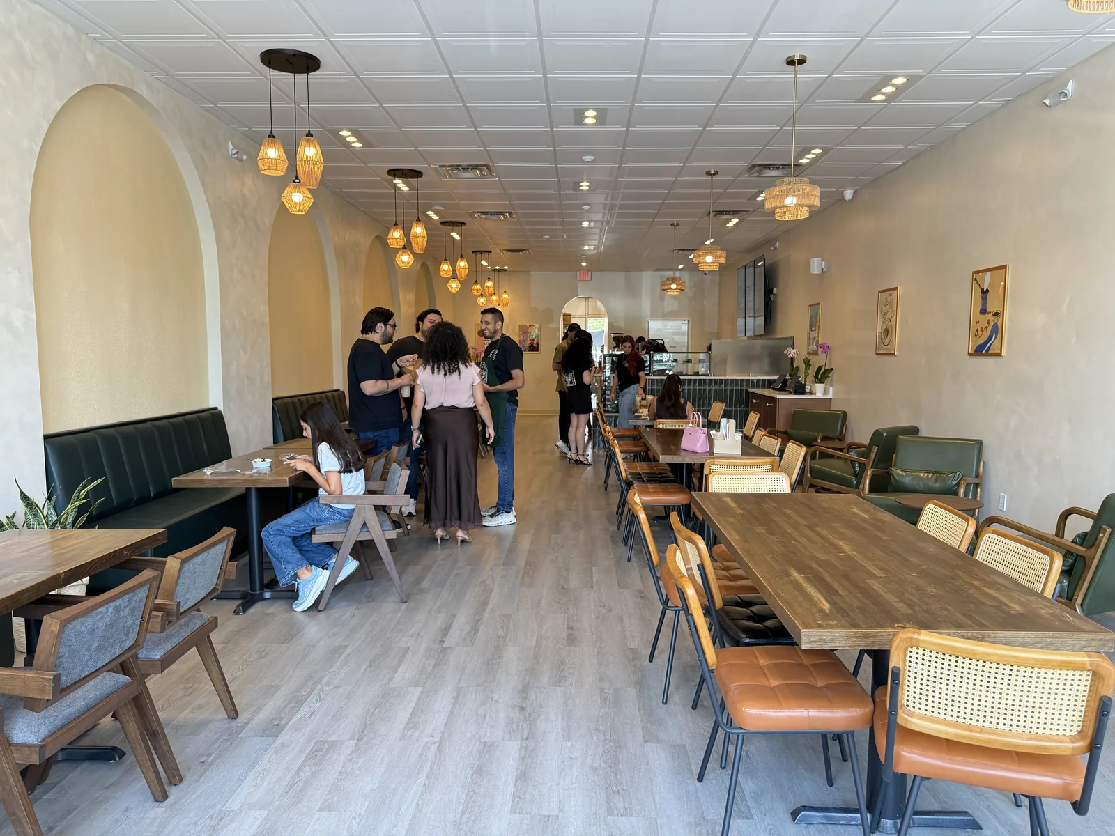 Guests ordering inside Habibi House Cafe in Falls Church, with arched alcoves, rattan pendant lights, green banquettes and long communal tables