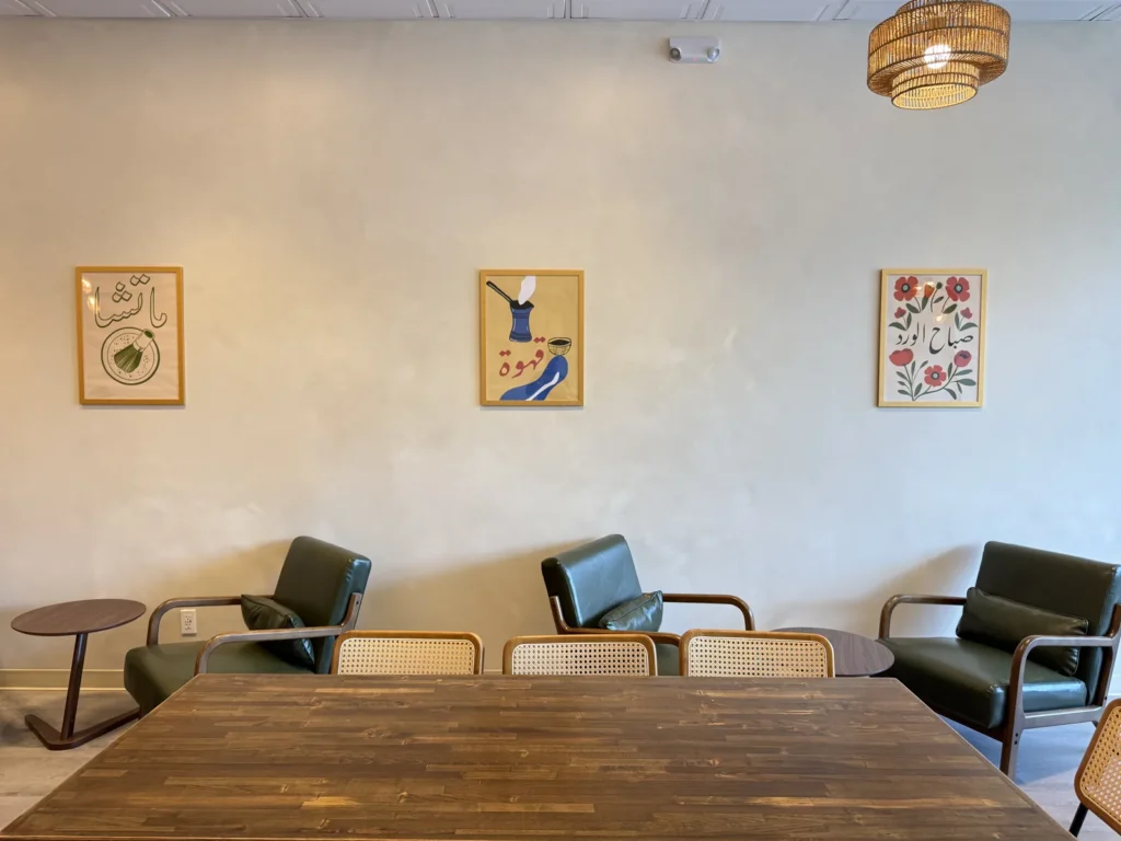 Seating nook at Habibi House Cafe with three framed Arabic calligraphy prints above green leather armchairs and cane chairs