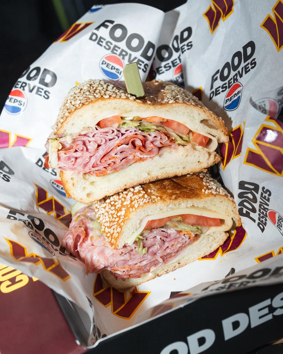 Two halves of a Capo Deli Italian sandwich with meats, cheese, lettuce and tomato