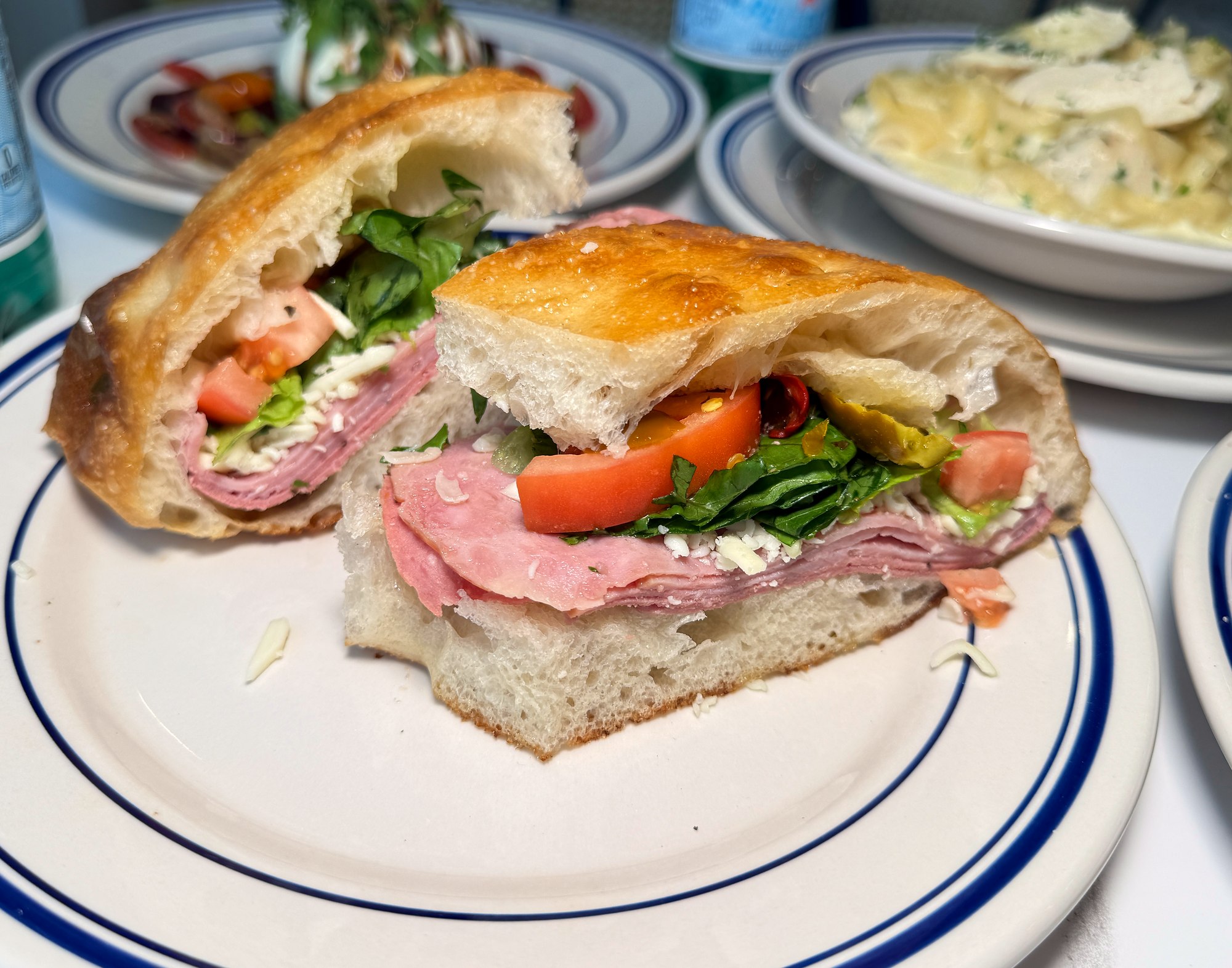 A sliced focaccia sandwich with meat, cheese, lettuce and tomato at La Pâte