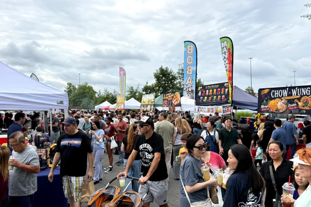 Crowds walking between food tents and boba and mango banners in the Fair Oaks Mall parking lot in Fairfax during an Asian night market this season