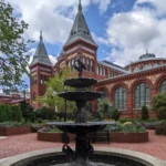 Red brick towers and arched windows of the Smithsonian Arts and Industries Building on the National Mall, seen from its garden fountain