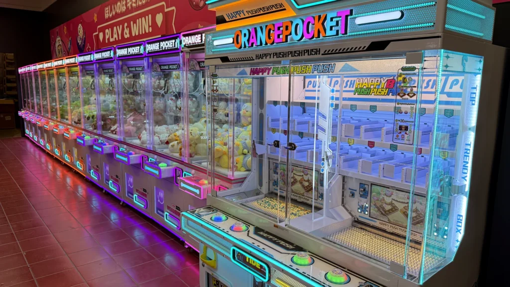 A row of lit claw machines inside Orange Pocket at Rio Lakefront, with an Orange Pocket sign above them