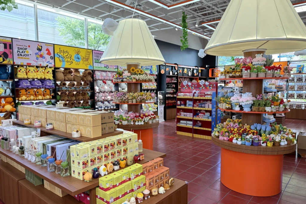 Inside Orange Pocket at Rio Lakefront in Gaithersburg before opening: tables of blind boxes and plush under lamp-shade lights, with Pokemon plush and snack shelves along the walls
