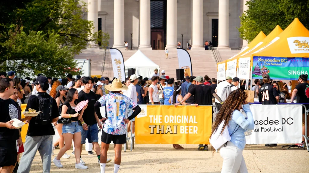 A row of white food vendor tents with a Singha banner and festivalgoers at the 2025 Sawasdee DC Thai Festival on the National Mall