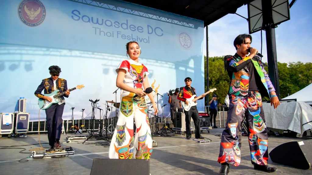 A Thai pop band in colorful printed suits playing guitars on the Sawasdee DC Thai Festival stage