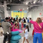 Visitors stretching colorful slime at Sloomoo Institute in Tysons Corner Center, with Sloomoo Falls in the background
