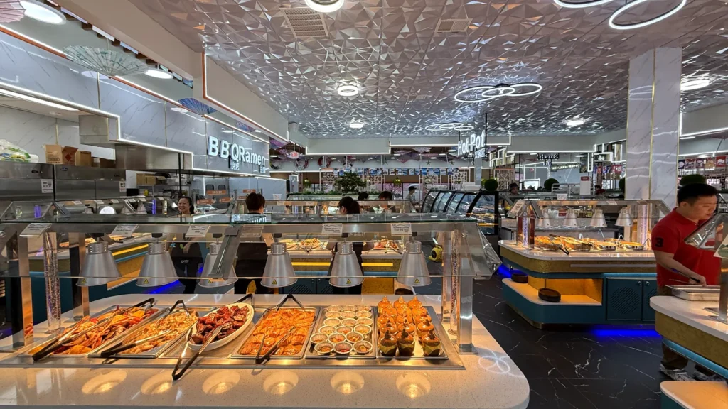 The buffet line inside UMI Alexandria, with heated trays under a mirrored ceiling and the BBQ and ramen counters behind