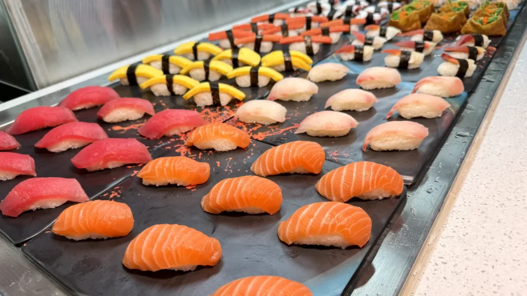 Salmon, tuna, white fish and tamago nigiri lined up on the sushi bar at UMI Alexandria, with inari and rolls behind