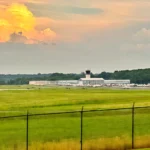 Runway and hangars at Washington Manassas Airport in Virginia under a wide summer sky, seen across the airfield grass