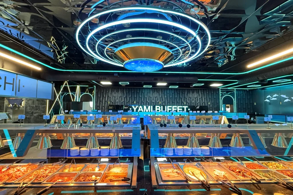 Inside Yami Buffet in Alexandria: a long buffet line under a blue neon ring light, with a lit Yami Buffet sign on the back wall