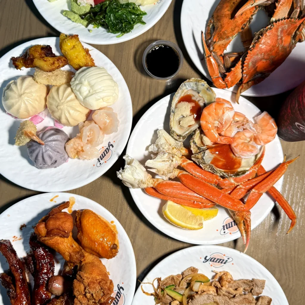A table of plates at Yami Buffet: whole blue crab, snow crab legs, sashimi, shrimp cocktail, steamed buns and ribs
