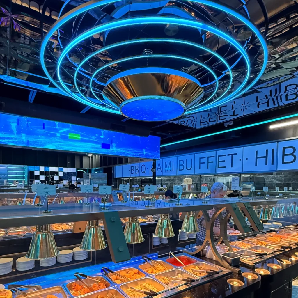 The blue neon ring light over the buffet line at Yami Buffet, with stacked plates and hot trays below