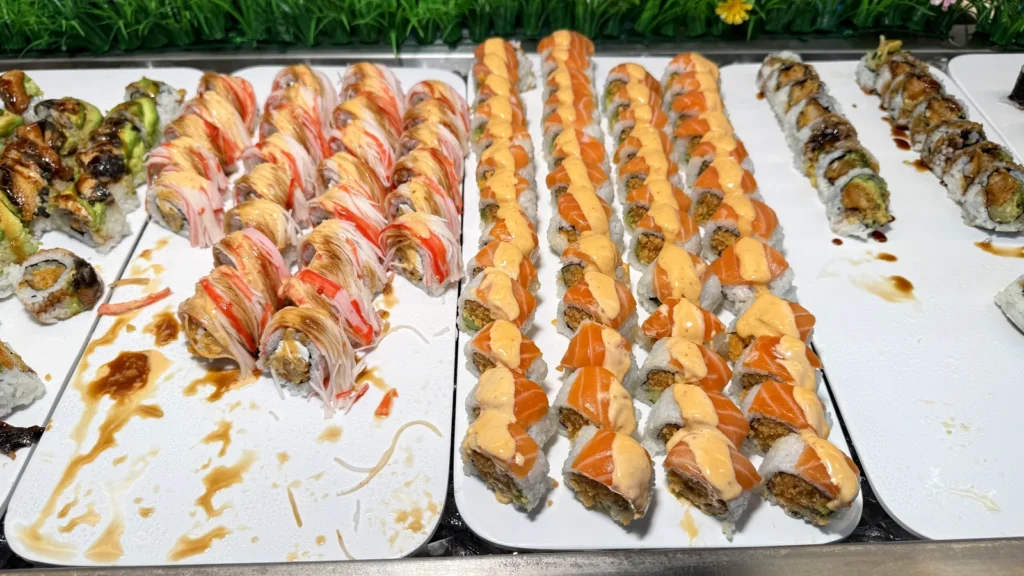 Rows of specialty sushi rolls topped with torched salmon, tuna and sauce on the Yami Buffet sushi line